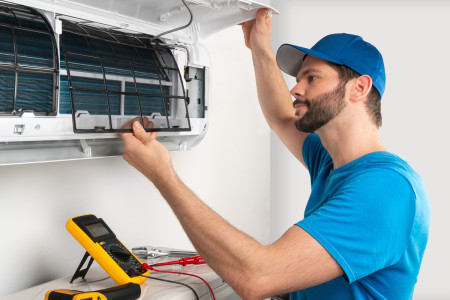 A man in a blue shirt repairing a wall AC unit in El Paso.
