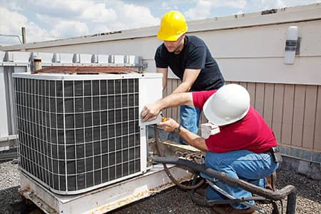 Technicians repairing an outdoor HVAC unit on a rooftop.
