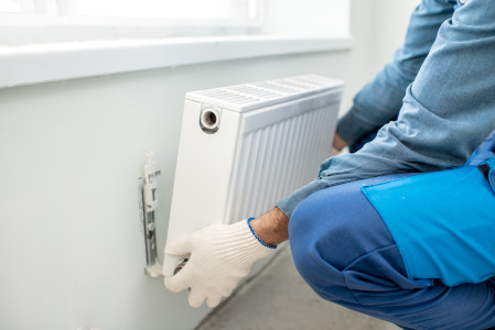 A person with gloves is installing a new heating unit into the wall of an El Paso home.