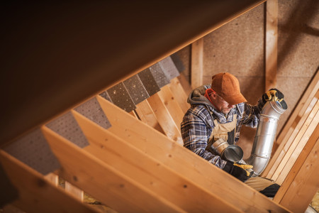 HVAC installer working on duct system in attic during home construction