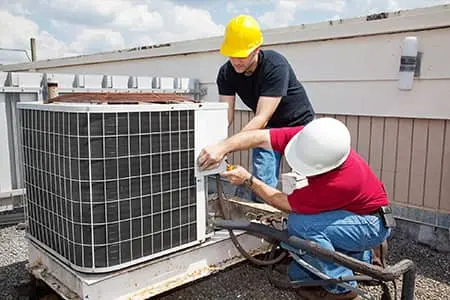 Technicians repairing an outdoor HVAC unit on a rooftop.