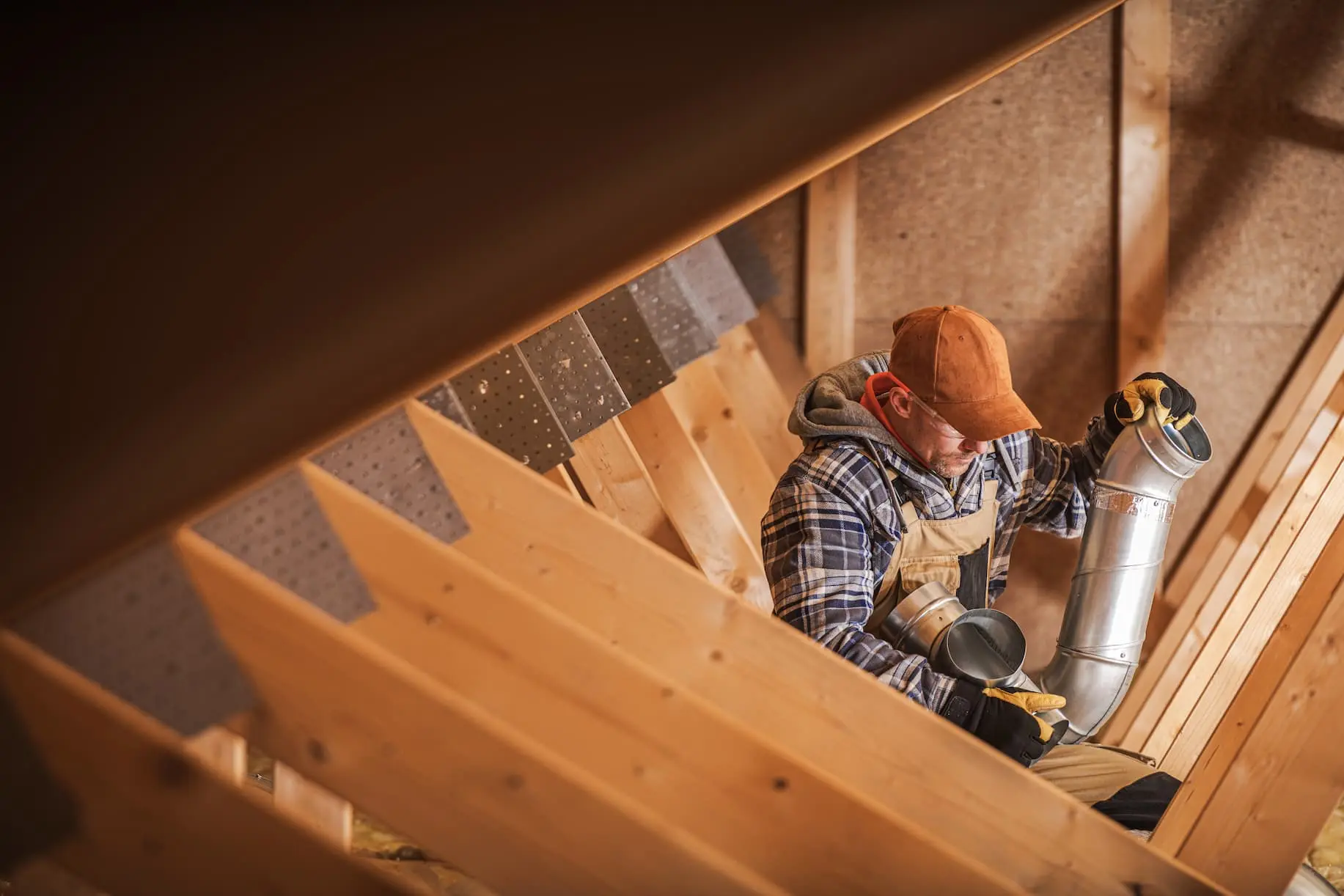 HVAC installer working on duct system in attic during home construction