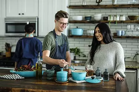 A man and woman cooking while enjoying their air conditioned home.