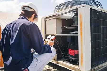 Worker performing AC Maintenance on an air conditioning unit.