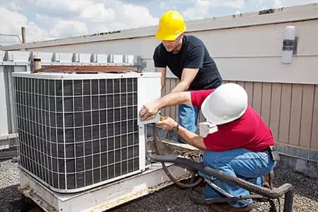 Two men performing hvac services on an air conditioning unit.