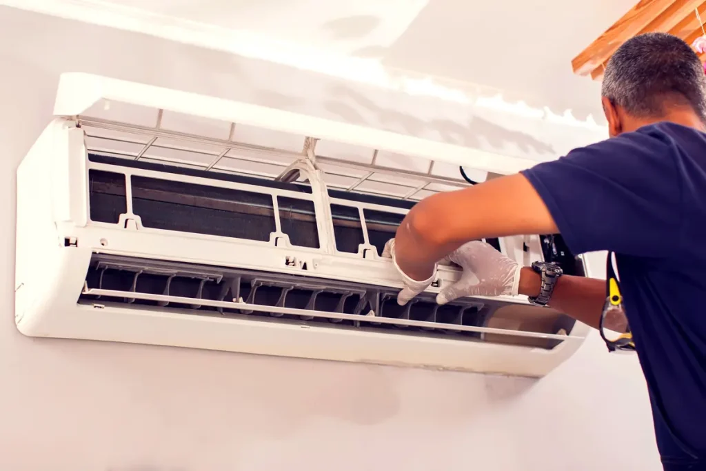 A man in a blue shirt installing a wall AC unit in an El Paso home.